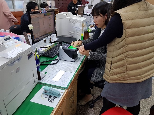 주민센터에서 지문스캐너를 이용해 지문등록을 하고 있는 직원과 민원인.