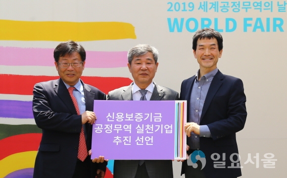조경식 신용보증기금 이사(가운데)가 김경민 한국공정무역협의회 대표이사(왼쪽), 이강백 한국공정무역마을위원회 위원장(오른쪽)과 함께 11일(토) 서울숲에서 개최된 ‘2019년 세계 공정무역의 날 한국 페스티벌’에서 ‘공정무역 실천기업’ 추진을 선언하고 기념촬영을 하고 있다. 사진제공=신용보증기금