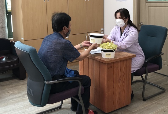 보건소 관계자가 한방진료실에 내방한 이용객들을 대상으로 콩나물 재배키트를 전달하고 재배법 등을 설명하고 있다.