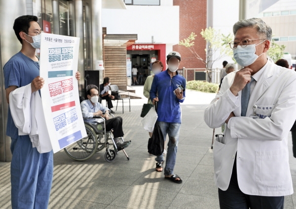 대한의사협회 2차 총파업을 하루 앞둔 지난 25일 오전 서울 종로구 서울대학교병원 본관 앞에서 김연수(오른쪽) 서울대병원장이 정부 의료정책에 반대하는 피켓을 들고 있는 서울대병원 전임의들을 바라보고 있다. [뉴시스]