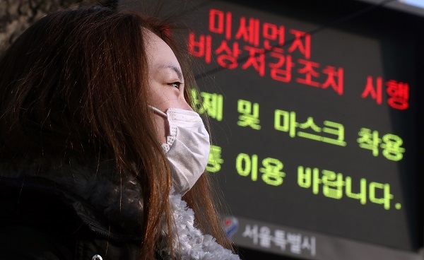 이틀째 고농도 미세먼지 예비저감조치가 발령된 지난 21일 오전 서울 중구 시청 인근에서 마스크를 착용한 시민 뒤로 예비저감조치 시행을 알리는 전광판이 보이고 있다. [뉴시스]