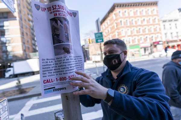 뉴욕시 경찰관이 전날 맨해튼 도심서 60대 아시아 여성을 폭행한 남성 용의자와 관련 정보를 제공하면 2500달러 제공의 수배자 전단을 붙이고 있다. [뉴시스]